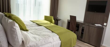 A hotel room with a large bed, a desk, a chair, and a TV mounted on the wall.