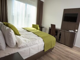 Quarto de hotel com uma cama grande, uma escrivaninha, uma cadeira e uma TV fixada na parede.
