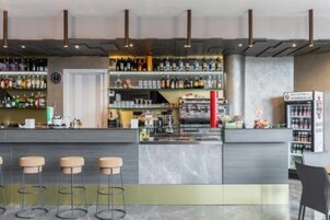 A modern bar area with a marble countertop, stools, and a variety of bottles and glasses.
