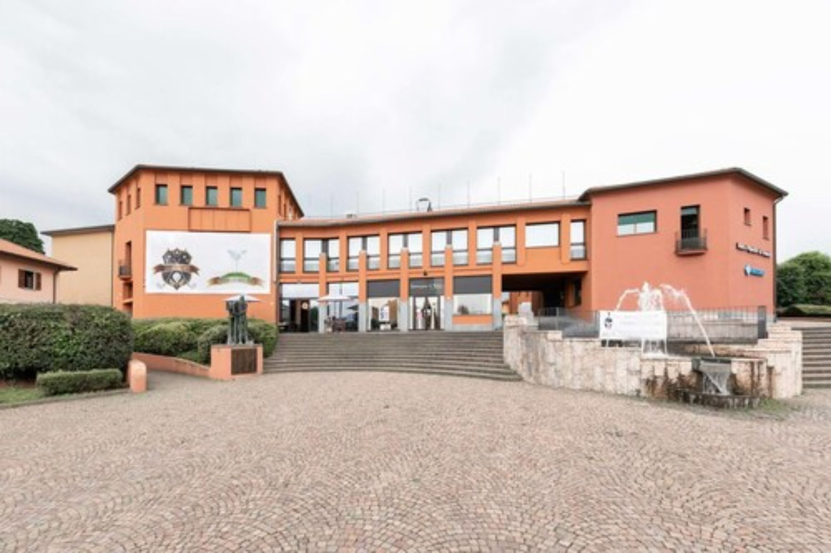 A building with a central entrance, a large banner, and a fountain in the courtyard.