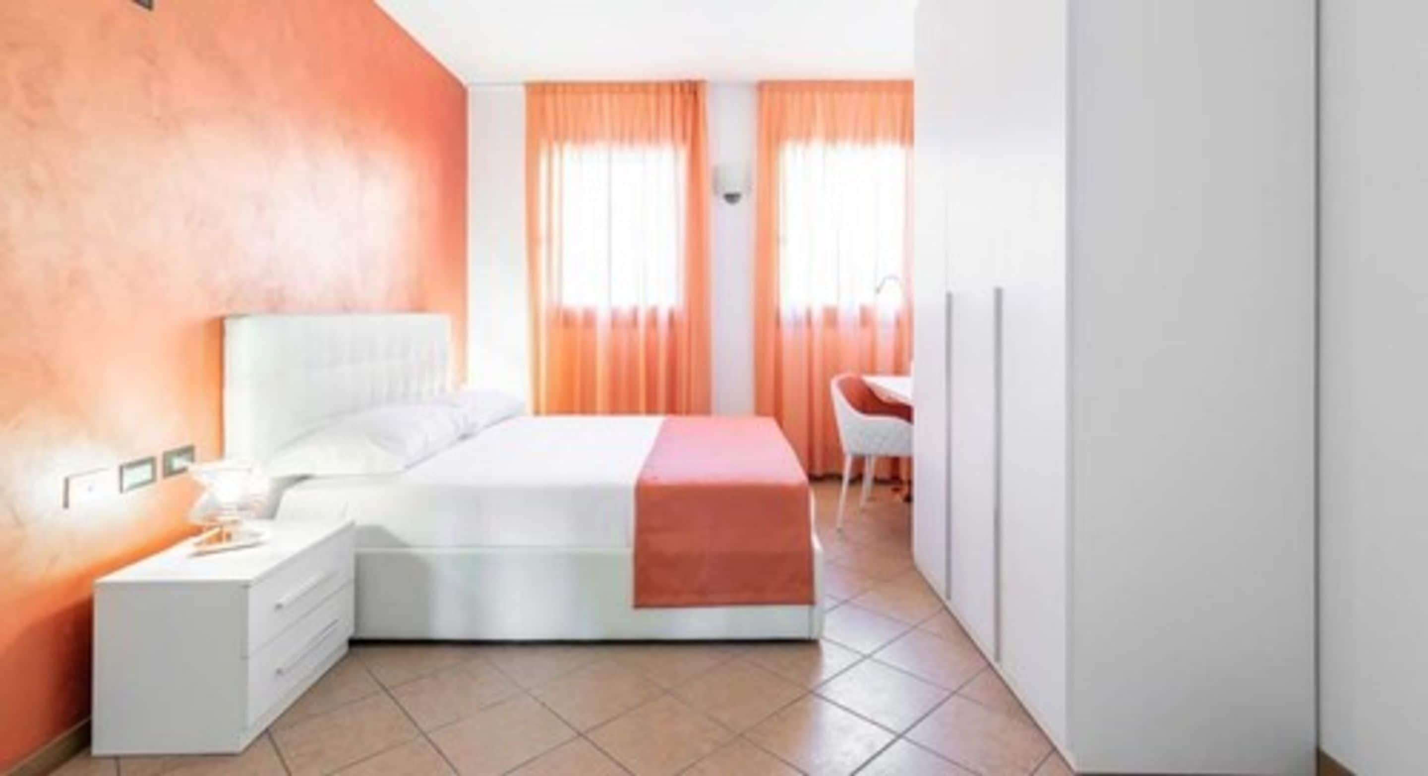 Ein modernes Schlafzimmer mit einem weißen Bett, orangefarbenen Vorhängen, einem weißen Schreibtisch und einem weißen Kleiderschrank.