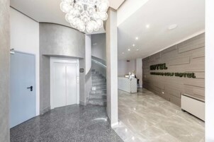 A modern hotel lobby with a marble floor, a staircase, and a reception desk.