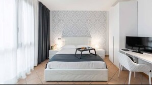 A modern hotel room with a bed, a desk with a TV, and a small table with a lamp. - Lake Como Golf Hotel (Carimate)