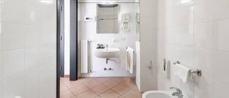 Un baño moderno con azulejos blancos, un lavamanos, un espejo y una zona de ducha.