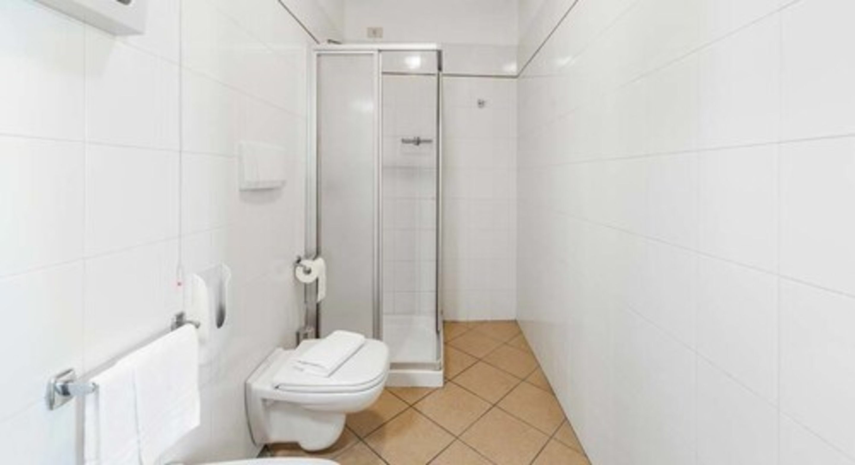 Un baño pequeño y moderno con azulejos blancos, inodoro, cabina de ducha de vidrio y barra para toallas.