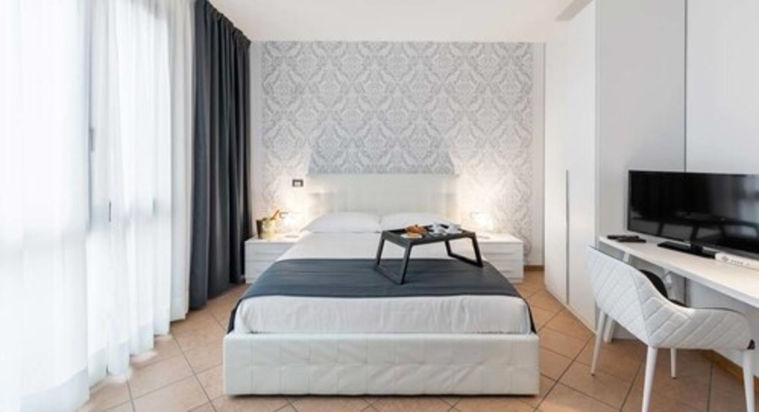 Una habitació d'hotel moderna amb un llit gran, un escriptori, una televisió i un paper pintat amb un disseny.