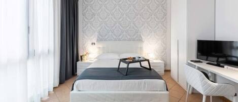 Una habitación de hotel moderna con una cama grande, un escritorio, un televisor y un papel tapiz estampado.