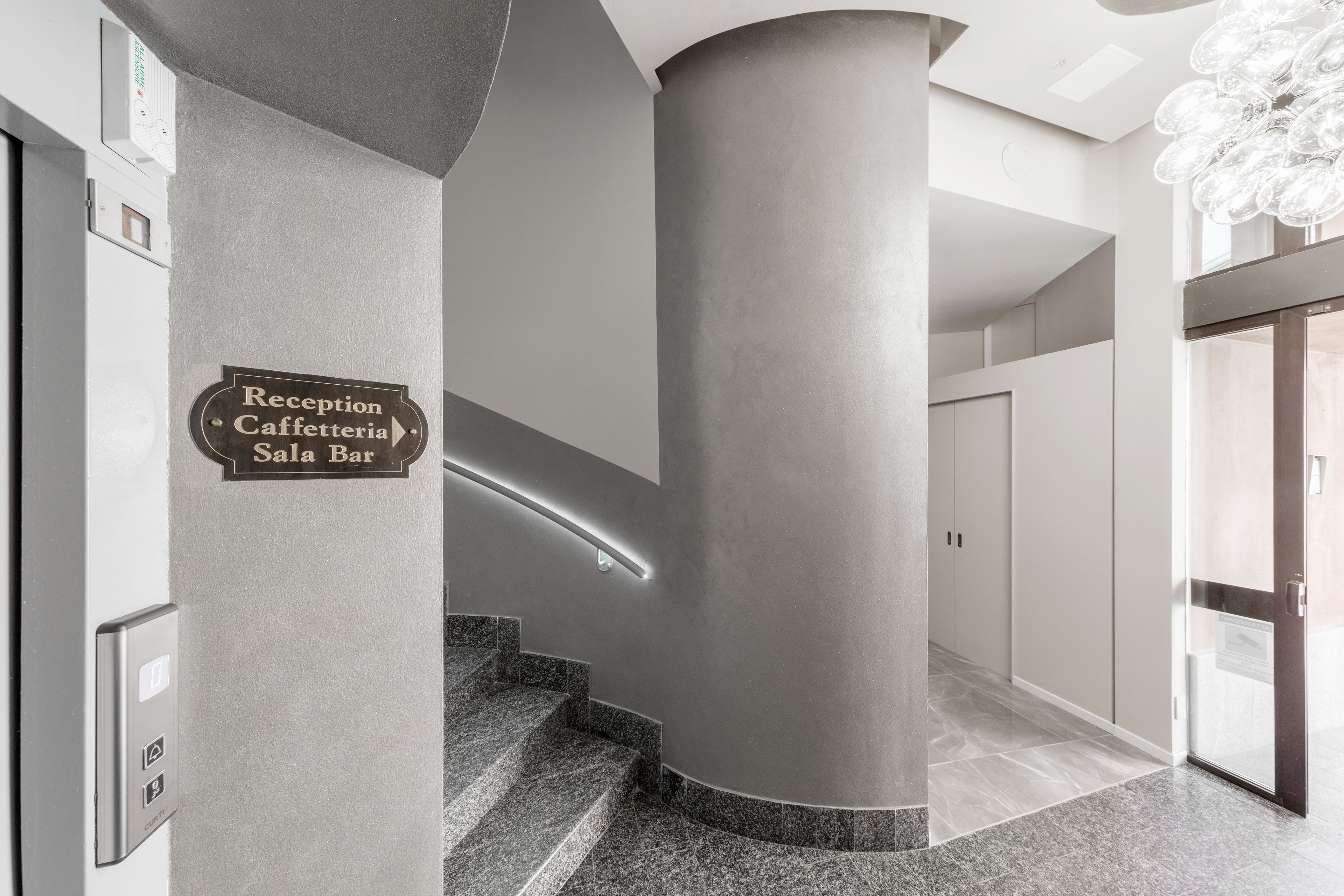 A reception area with a sign for the Reception Caffetteria Sala Bar, a curved staircase, and a modern light fixture.