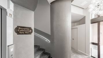 A reception area with a sign for the Reception Caffetteria Sala Bar, a curved staircase, and a modern light fixture.