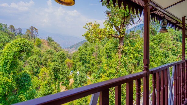 A balcony with a view of a lush green valley and mountains in the distance.