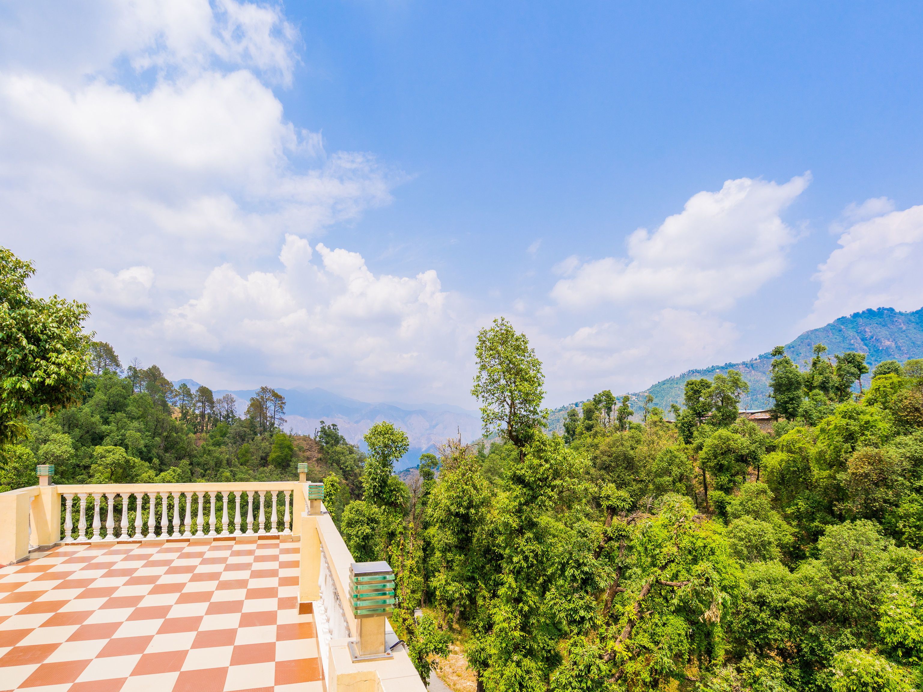 A terrace with a checkered floor and a white balustrade, surrounded by lush greenery and a mountain in the background.