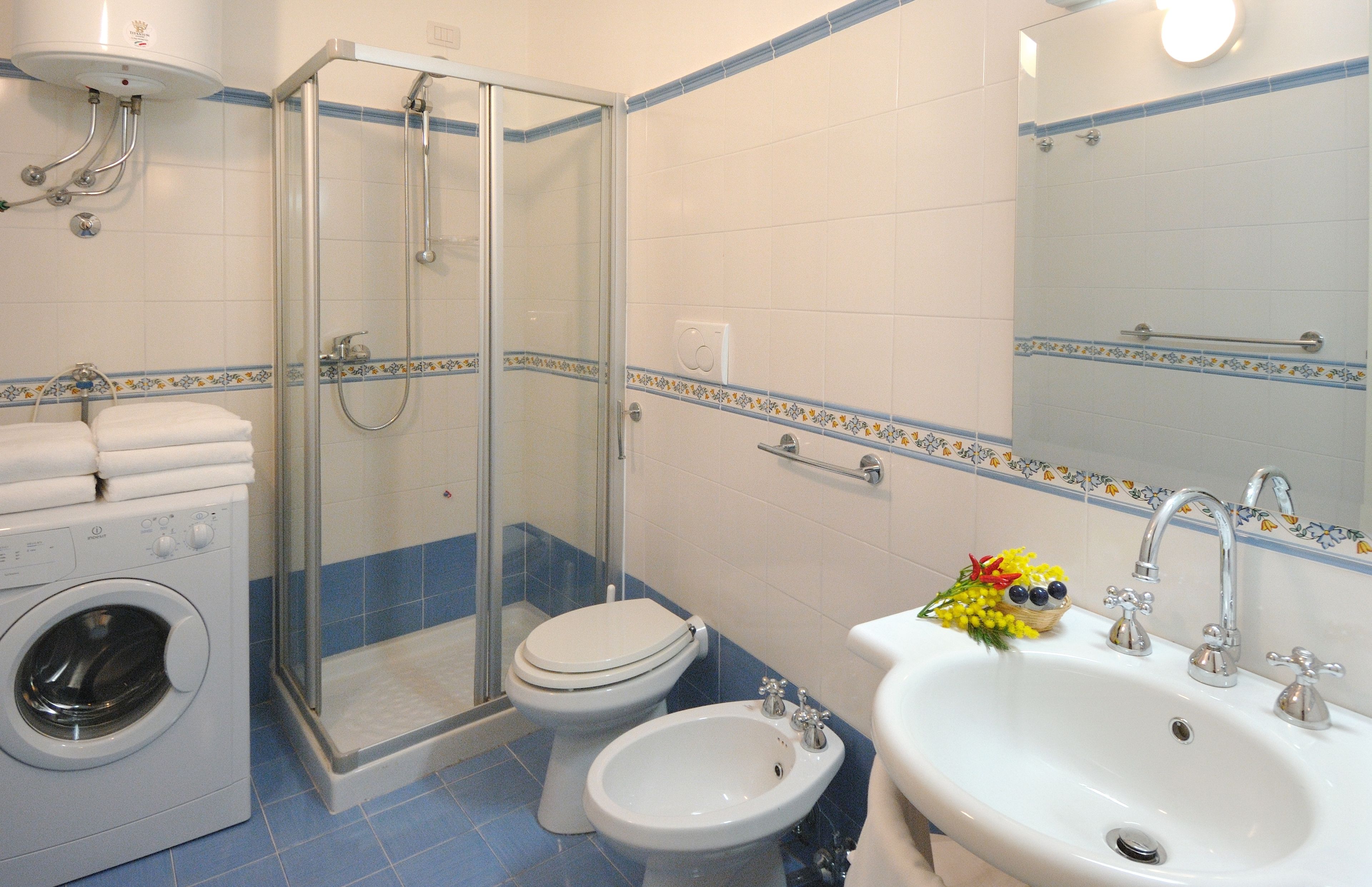 A bathroom with a glass-enclosed shower, a toilet, a bidet, a sink, and a washing machine.