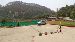 A parking area with a car, potted plants, and a view of terraced fields and buildings on a hillside. - OYO 13756 Damyanty Residency & Resort (Nainital)