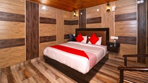A wooden-paneled bedroom with a large bed, red pillows, a nightstand, and a chair. - OYO 13756 Damyanty Residency & Resort (Nainital)