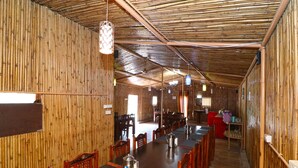 A bamboo-paneled dining area with wooden tables and chairs, a coffee pot, and hanging light fixtures. - OYO 13756 Damyanty Residency & Resort (Nainital)