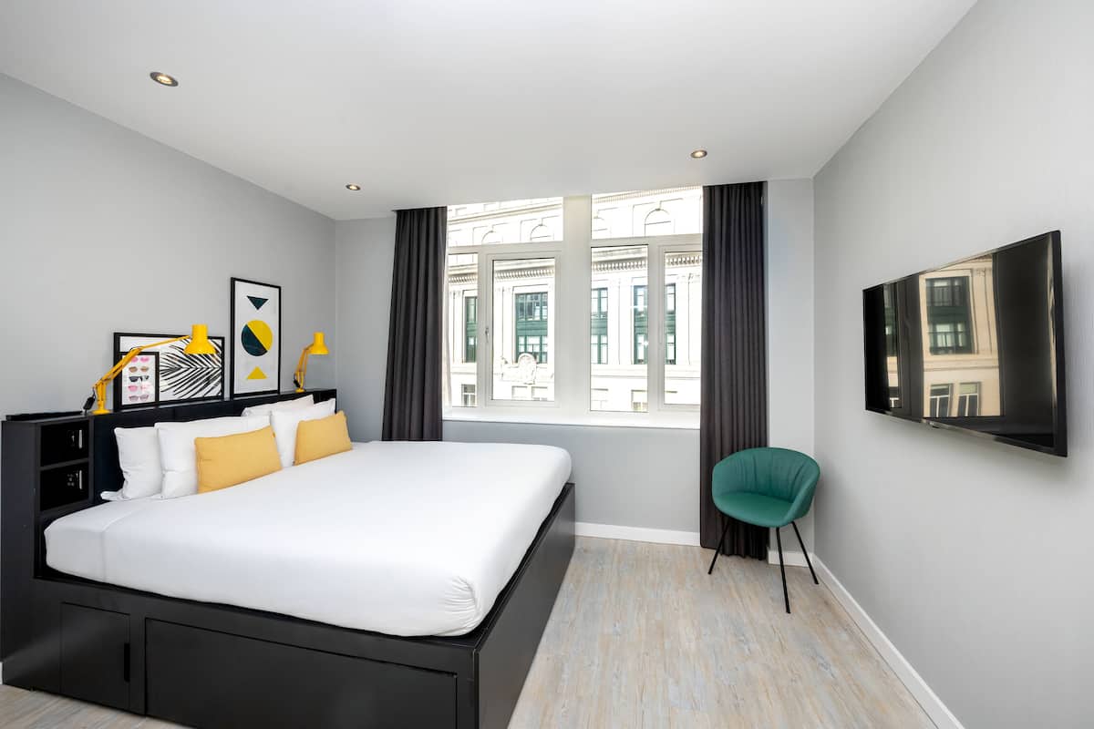 A modern hotel room with a large bed, a TV mounted on the wall, and a window with curtains.