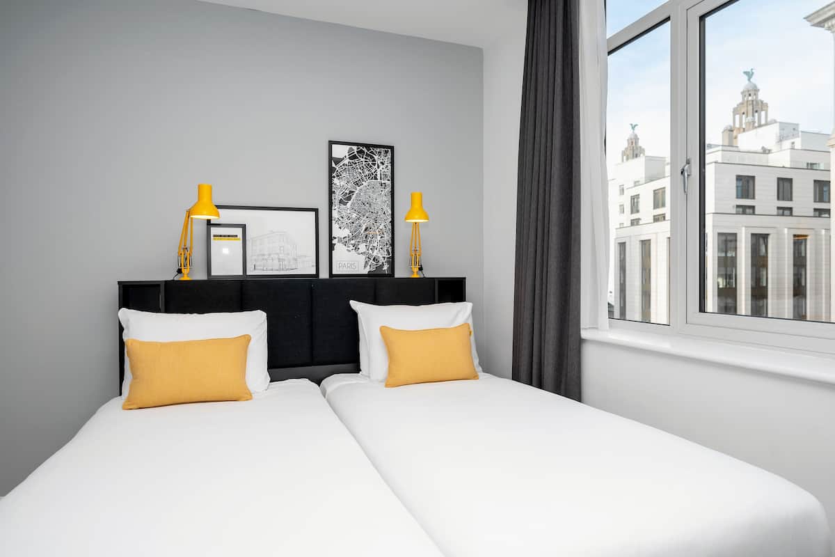 A hotel room with a bed, two pillows, two lamps, and two framed pictures on the headboard.