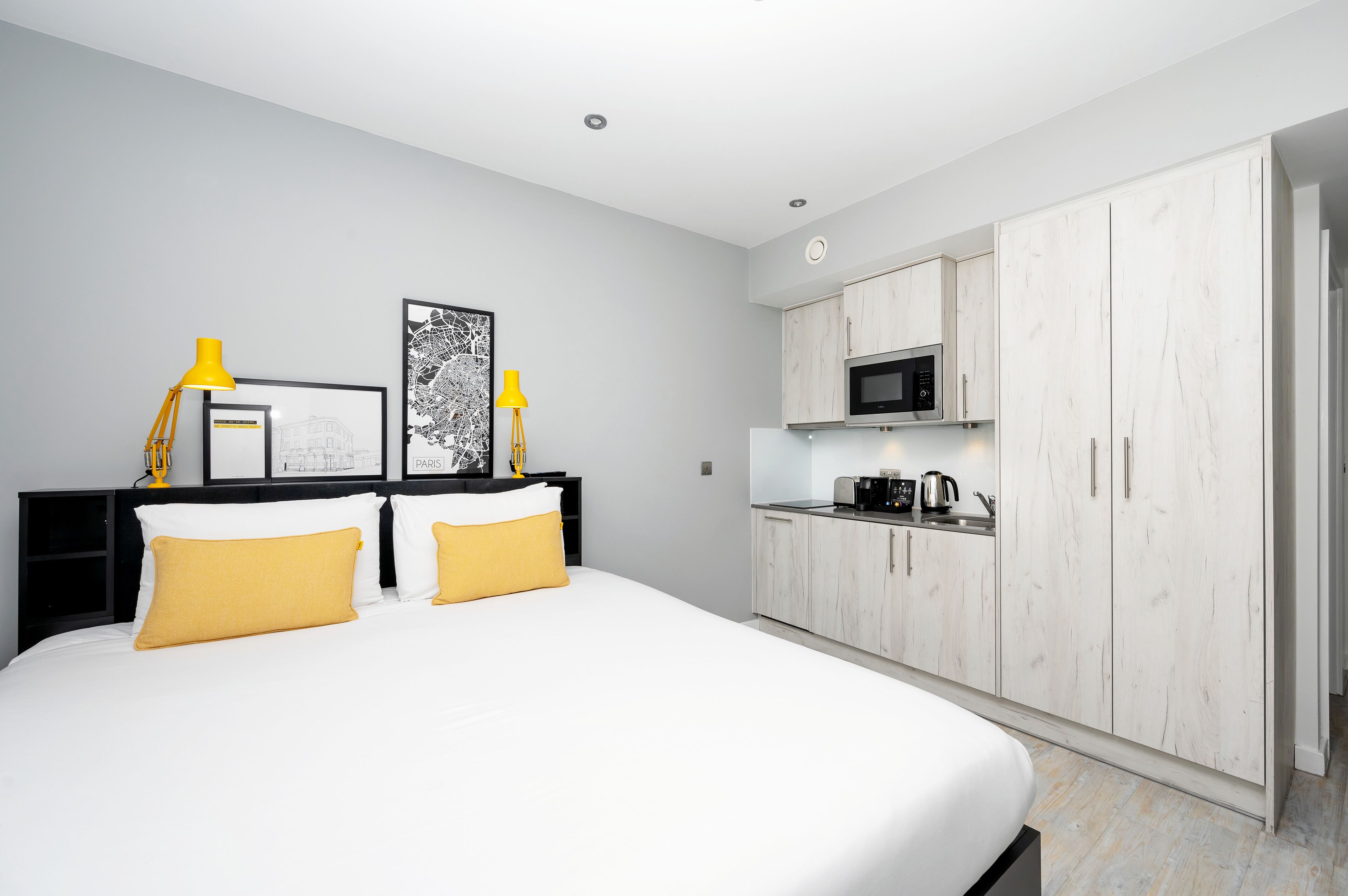A modern hotel room with a large bed, a small kitchenette, and a wardrobe.