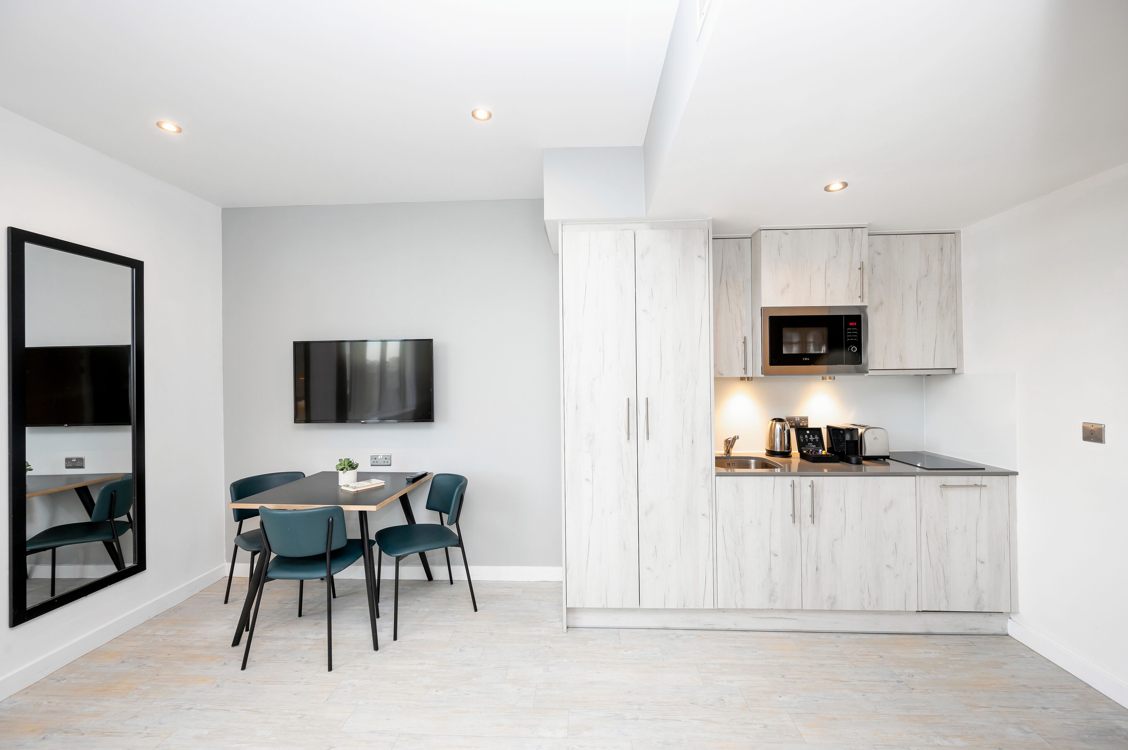 A modern kitchen with white cabinetry, a built-in microwave, and a dining area with a table and chairs.