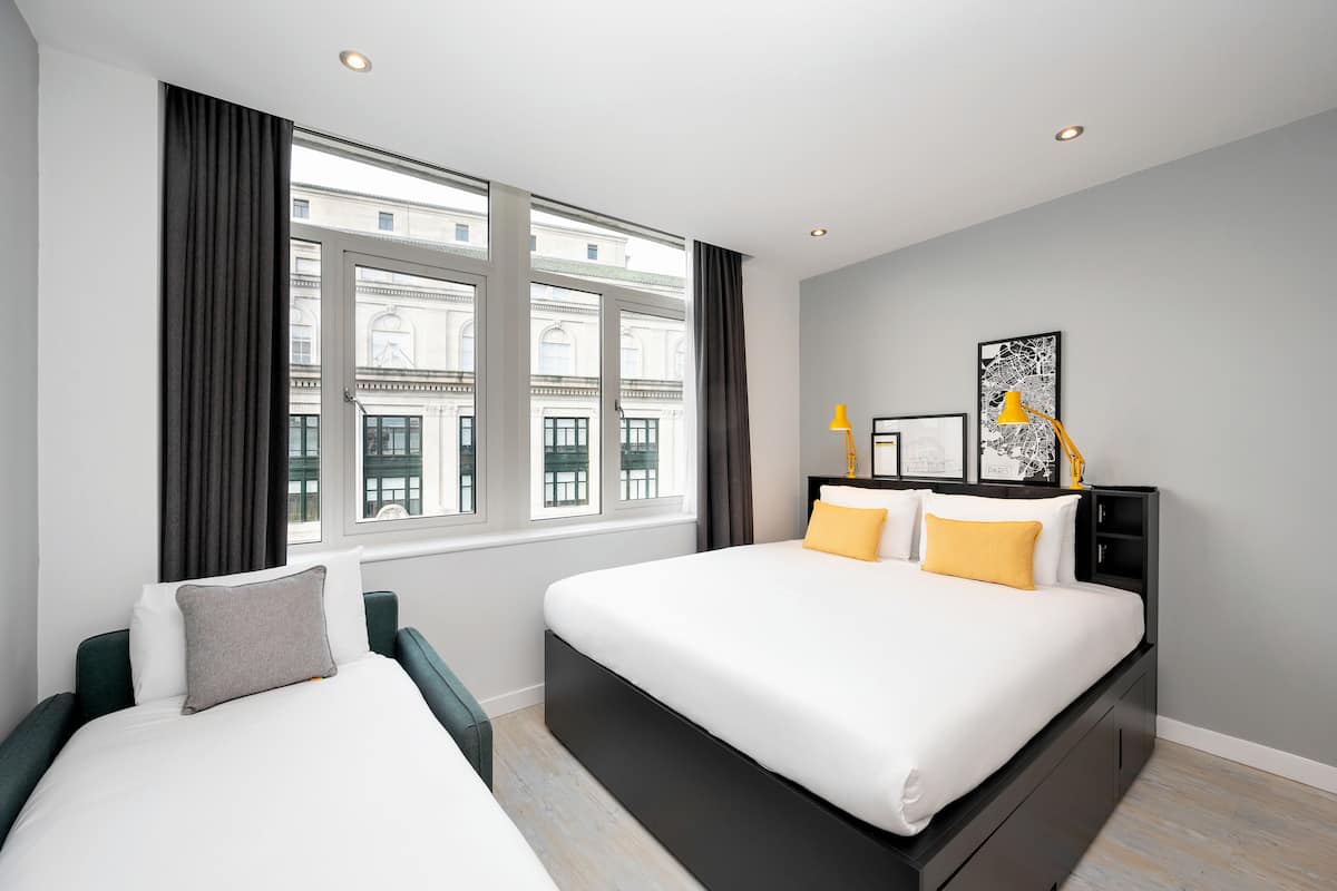 A modern hotel room with a large bed, a bedside table, a chair, and a window with curtains.