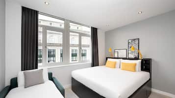 A modern hotel room with a large bed, a bedside table, a chair, and a window with curtains.