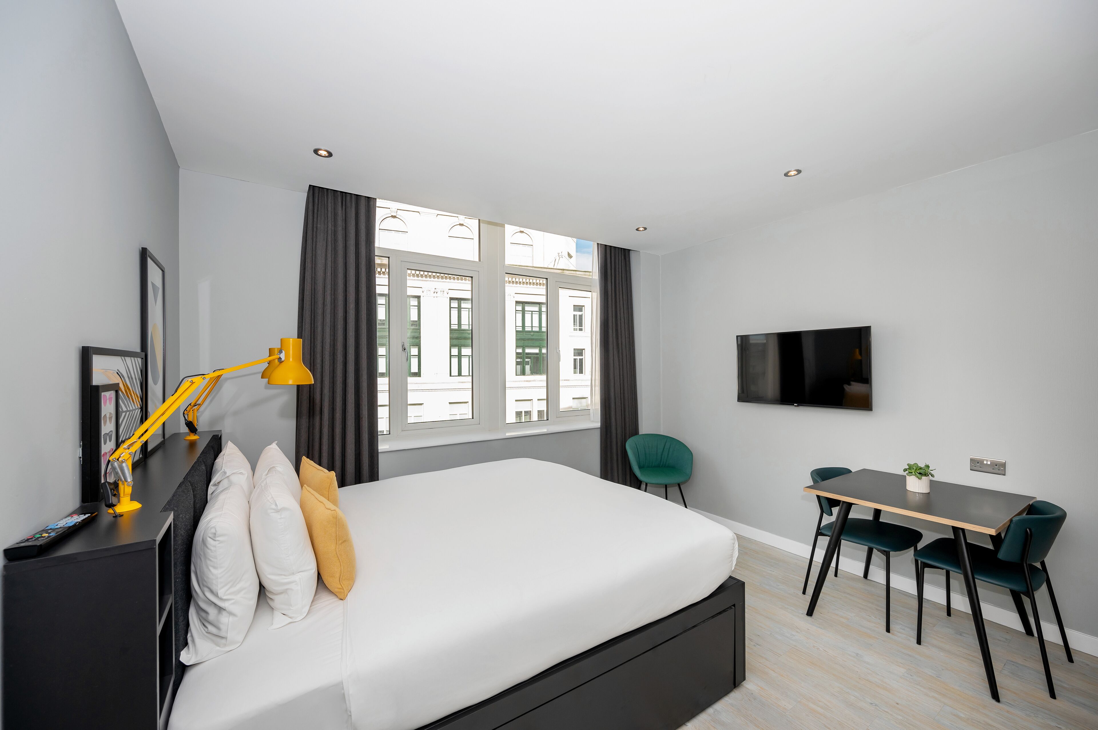 A modern hotel room with a large bed, a desk with two chairs, a TV, and a window with curtains.