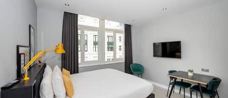 A modern hotel room with a large bed, a desk with two chairs, a TV, and a window with curtains.