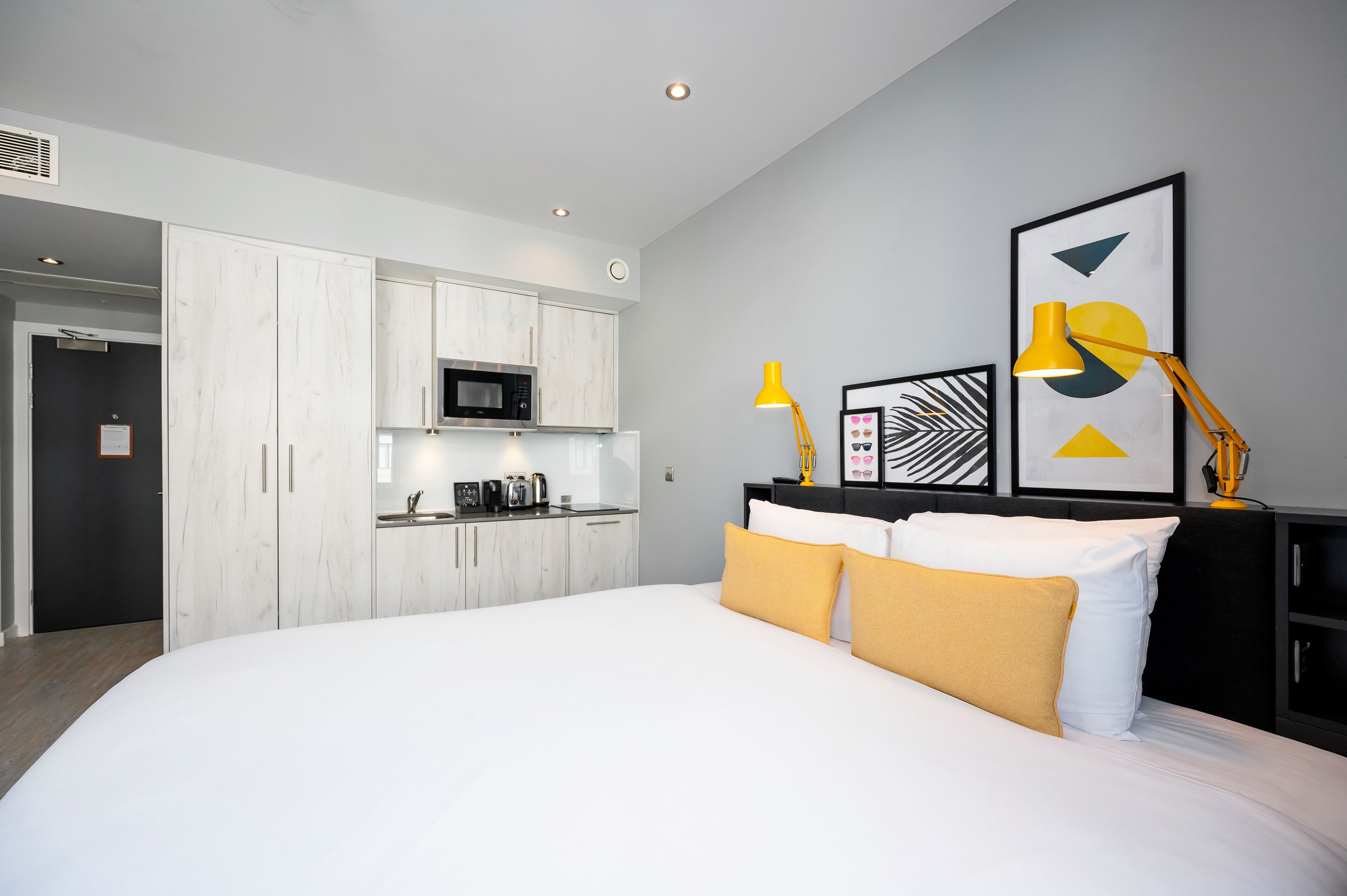 Quarto de hotel moderno com uma cama grande, uma kitchenette e uma área de refeições.