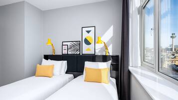 A modern hotel room with two beds, a large window with a city view, and decorative wall art.
