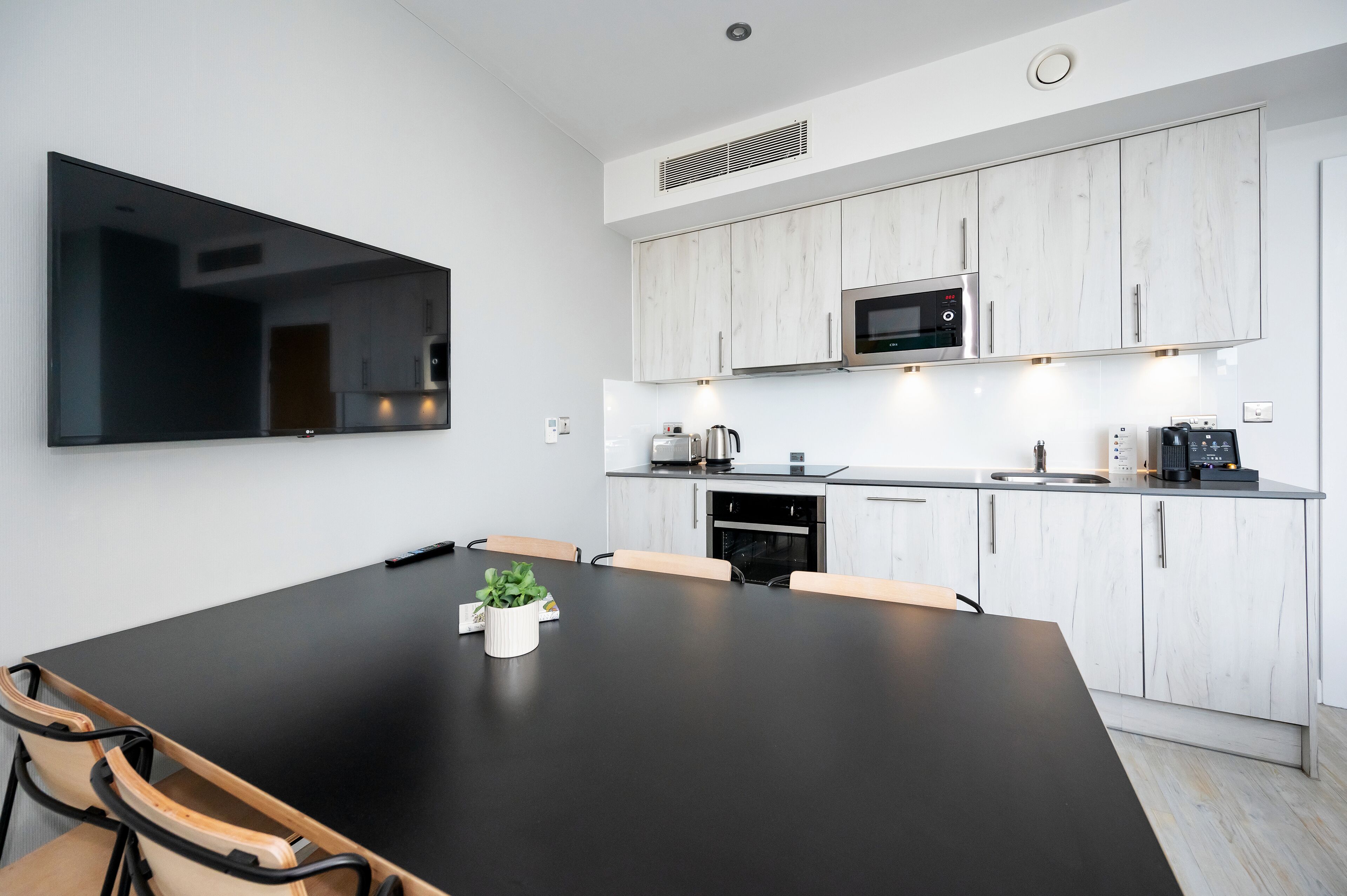 A modern kitchen with white cabinetry, a black countertop, and a large flat-screen TV mounted on the wall.