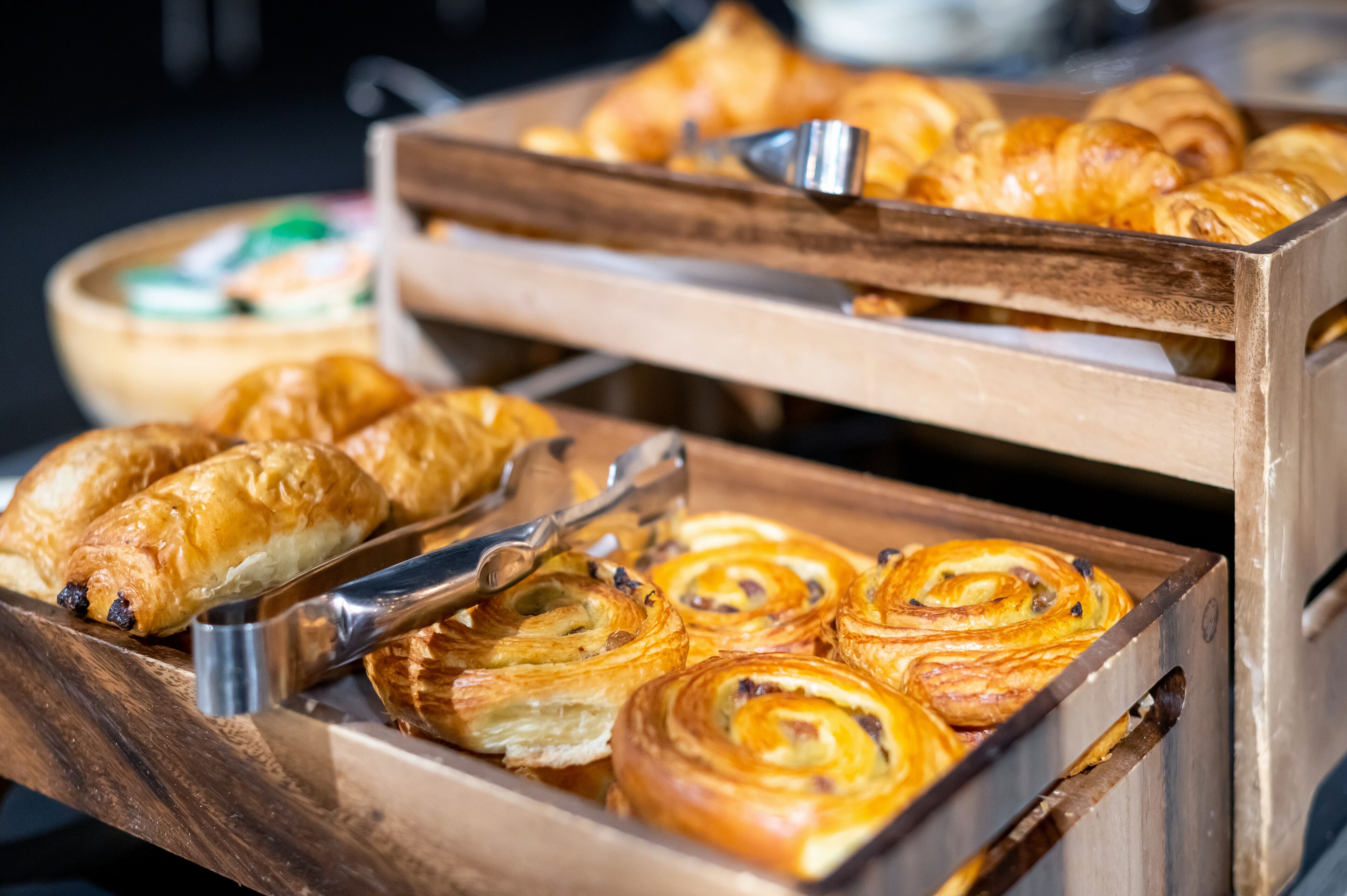 Una bandeja de madera con pastelería, incluyendo croissants y rollos de canela, dispuesta para servir.