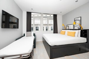 Una habitación de hotel moderna con una cama grande, una cama más pequeña, un televisor montado en la pared y una ventana con cortinas.