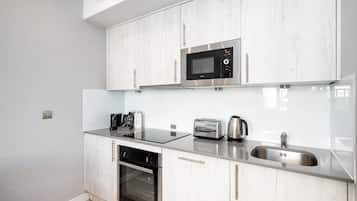Una cocina moderna con armarios blancos, microondas integrado, tostadora y pileta de acero inoxidable.