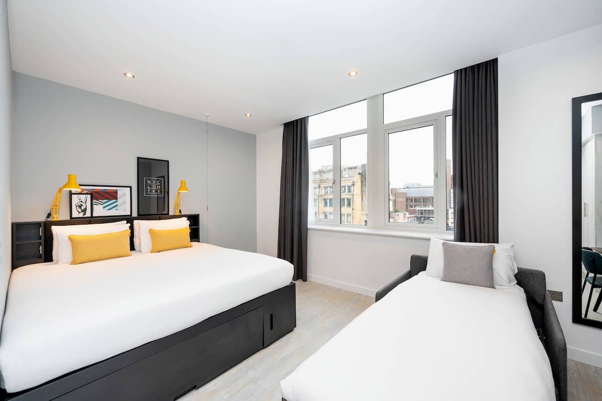 A modern hotel room with two beds, a large window with curtains, and a city view.