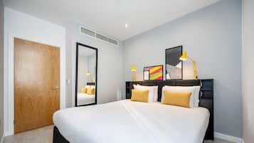 Una habitación de hotel moderna con una cama grande, una mesita de noche con lámpara, un espejo y un cuadro enmarcado en la pared.