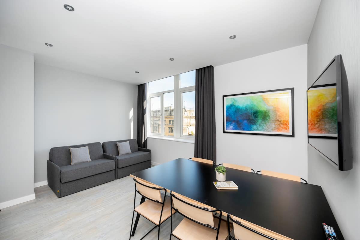 A modern meeting room with a black table, four chairs, a grey sofa, and a large window with curtains.