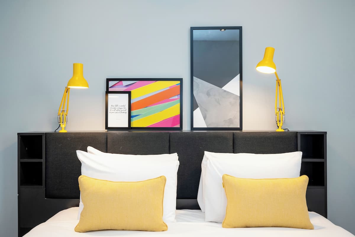A neatly made bed with white and yellow pillows, a black headboard, and two yellow bedside lamps.