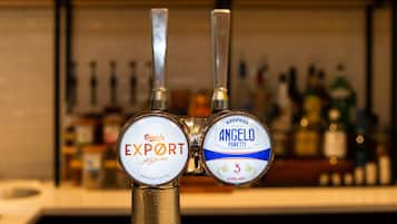 A tap with two beer labels, one for Carlsberg Export and one for Angelo Poretti, with a blurred background of bottles.
