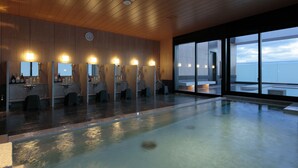 A modern indoor swimming pool with multiple shower stations, large windows offering a view of the sky, and a wooden ceiling. - Candeo Hotels Osaka Kishibe (Suita)