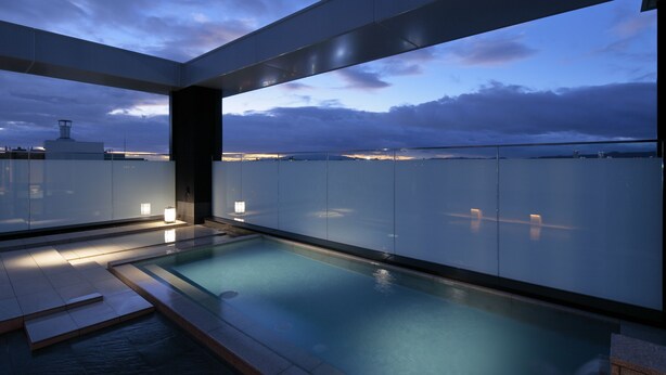 A rooftop infinity pool with a glass barrier, offering a view of the city skyline at dusk. - Candeo Hotels Osaka Kishibe (Suita)