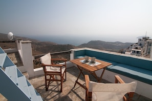 A terrace with a table and chairs, overlooking a hilly landscape.