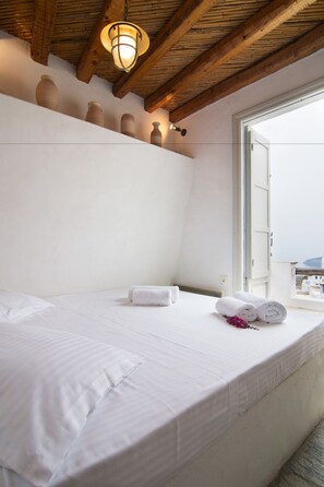 A bedroom with a bed, white linens, a wooden ceiling, and a window with a view.