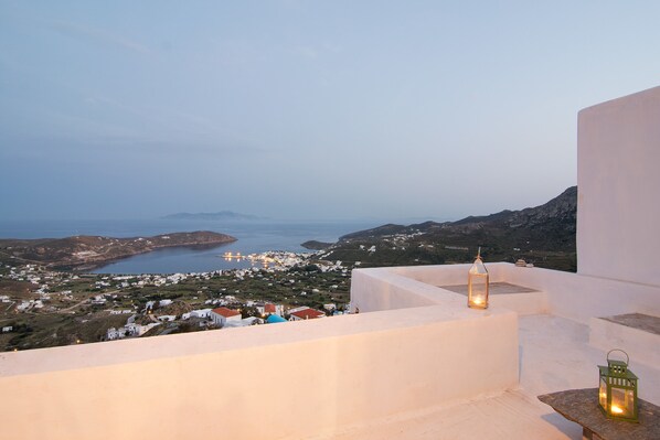 A coastal view with a white building, two lit lanterns, and a distant town.