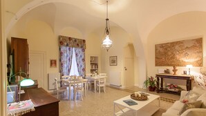 Ein geräumiges Wohnzimmer mit Essbereich, weißen Möbeln, einer Kristallleuchter und einem großen Gemälde an der Wand.