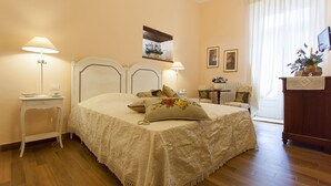 Ein Schlafzimmer mit Bett, Nachttischlampen, einem kleinen Tisch, einem Schminktisch und einem Fenster mit Vorhängen.