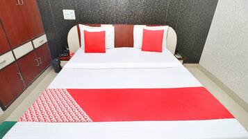 A hotel room with a bed, red and white bedding, a wooden wardrobe, and a nightstand with a phone and remote control.