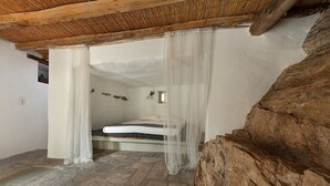 Ein rustikales Schlafzimmer mit Steinboden, einem Bett mit weißer Bettwäsche und einer Holzzielung.