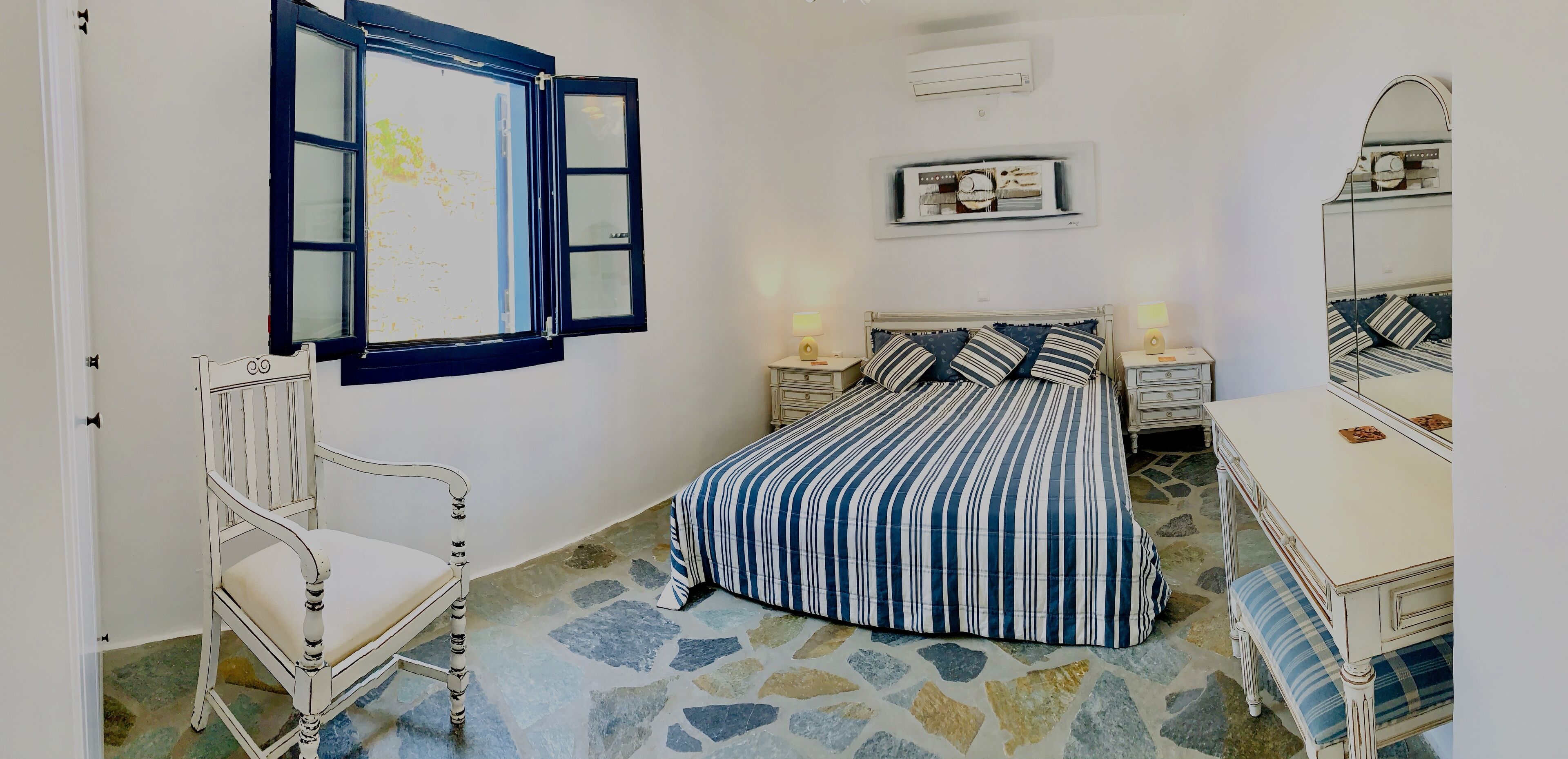 Une chambre à coucher comprenant un lit, une chaise, une commode, un miroir et un climatiseur fixé au mur.