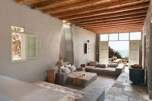 A spacious room with a high ceiling, built-in seating areas, and large windows offering a view of the sea. - Serifos Houses Aghios Sostis (Serifos)