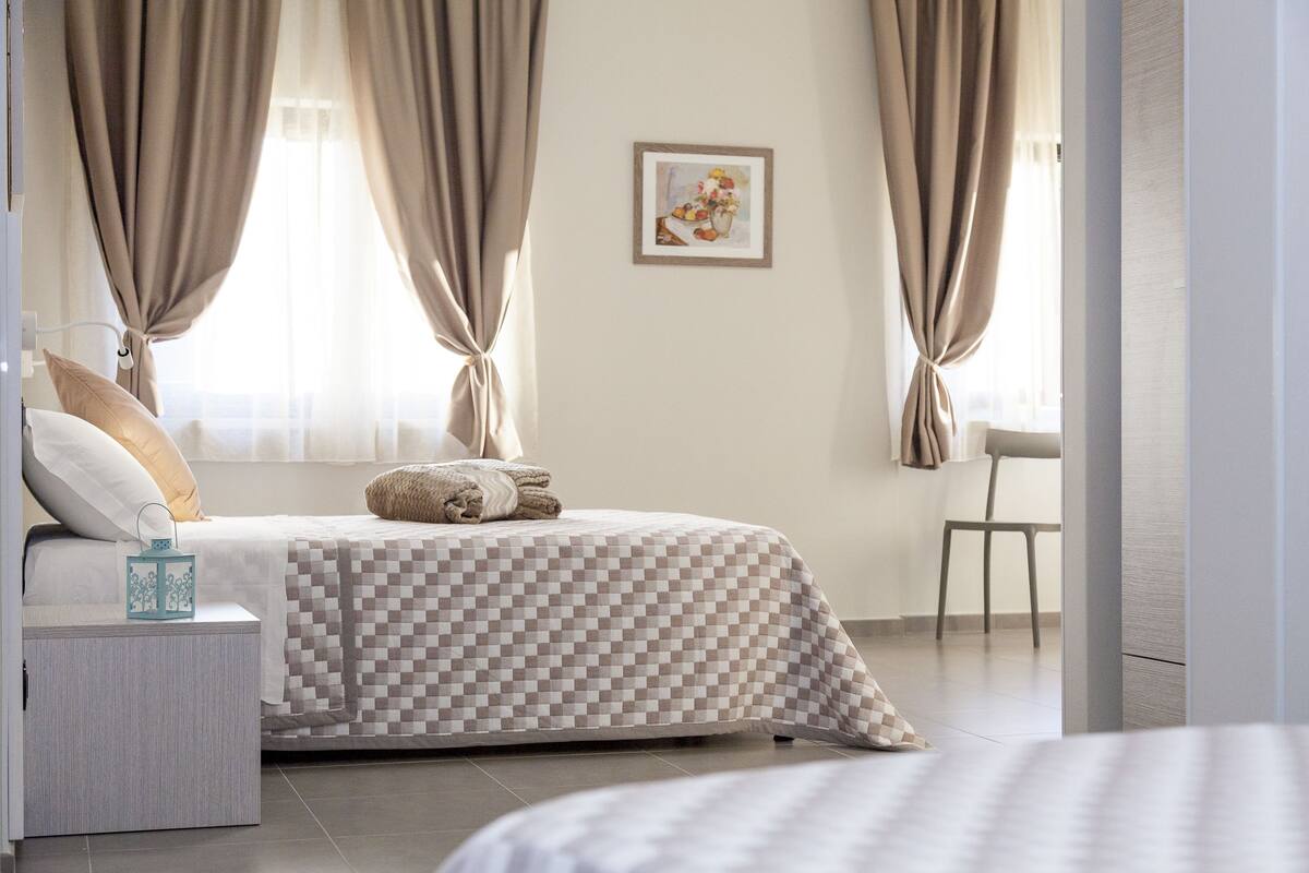 A bedroom with a checkered bedspread, a bedside table with a lamp, and a chair.